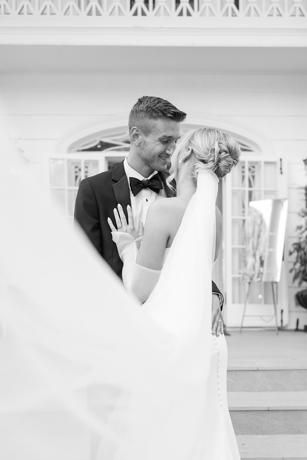 Black and white portrait of the couple sharing an intimate moment, framing them with the bride's soft veil.